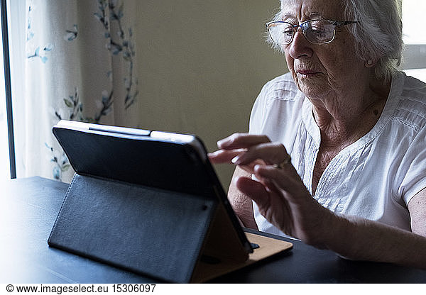 Close up of senior woman sitting at a table  using a digital tablet  using the touch screen.