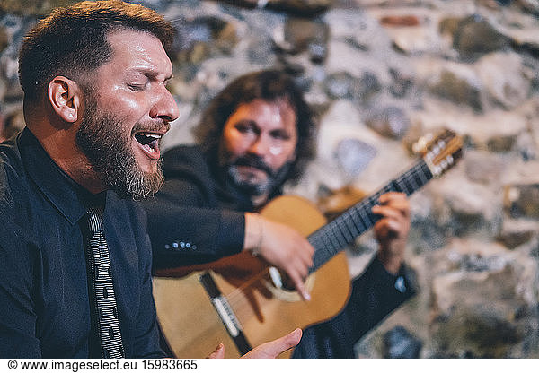 Close-up of singer with eyes closed singing while guitarist playing flamenco on guitar in background