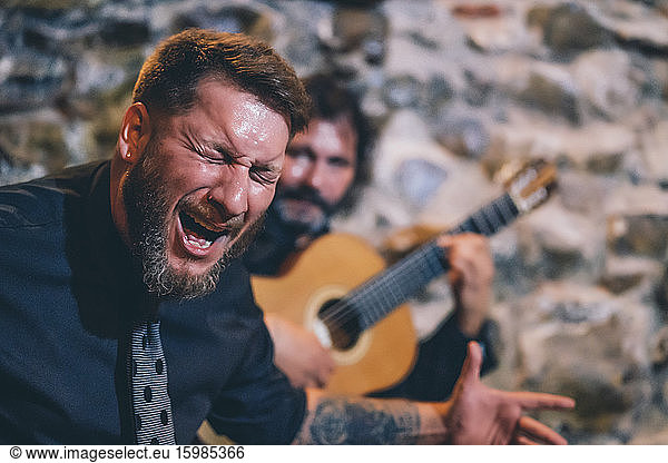 Close-up of singer with eyes closed singing while guitarist playing guitar in background