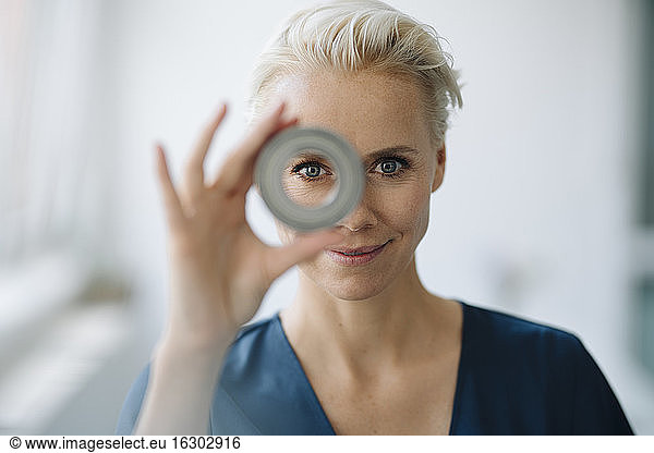 Close-up of smiling businesswoman looking through object in office