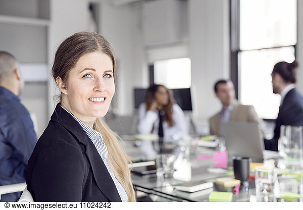 Close-up of smiling businesswoman sitting with colleagues at conference table