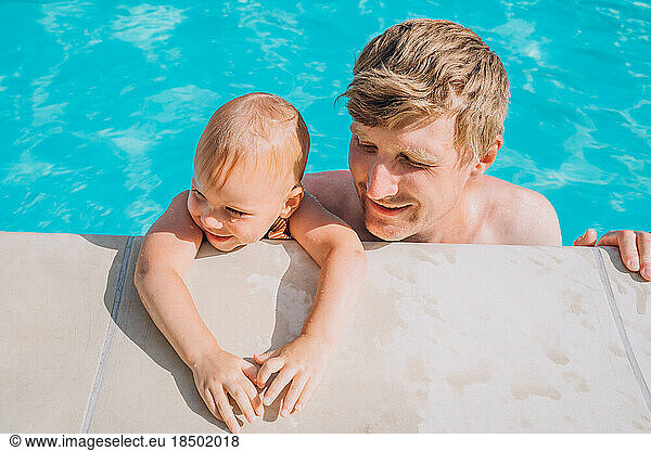 Close-up of smiling father and daughter by the side of the open pool