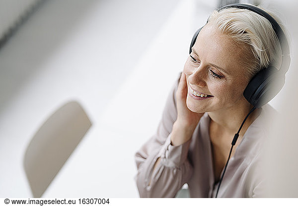 Close-up of smiling female professional listening music through headphones in office