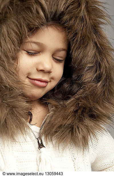 Close-up of smiling girl with closed eyes wearing fur hood