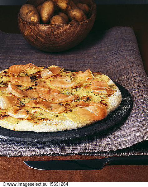 Close-up of smoked salmon pizza with potatoes in bowl on table