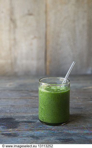 Close-up of smoothie served in drinking glass with straw on wooden table