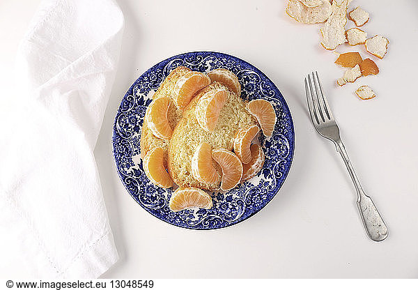 Close-up of sweet bread with oranges in plate over white background