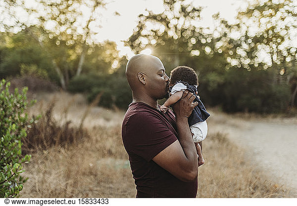 Close up of sweet father kissing newborn girl in backlit field