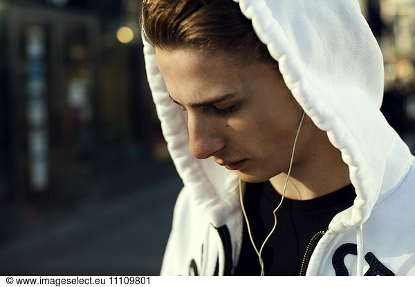 Close-up of teenage boy wearing hooded shirt listening music through headphones