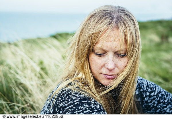 Close-up of thoughtful blond woman sitting on grassy field