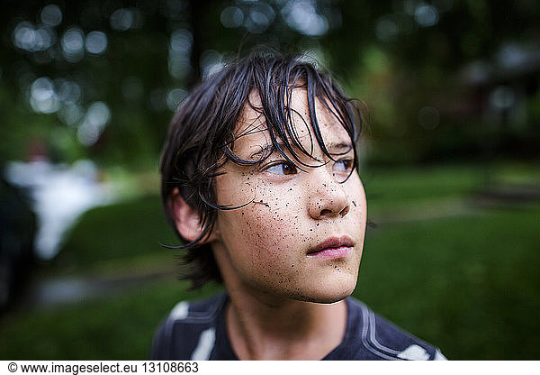Close-up of thoughtful boy with dirty face standing at yard during rainy season