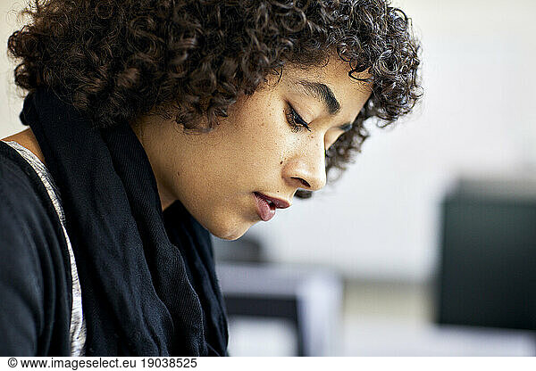 Close-up of thoughtful businesswoman with curly hair looking down in office