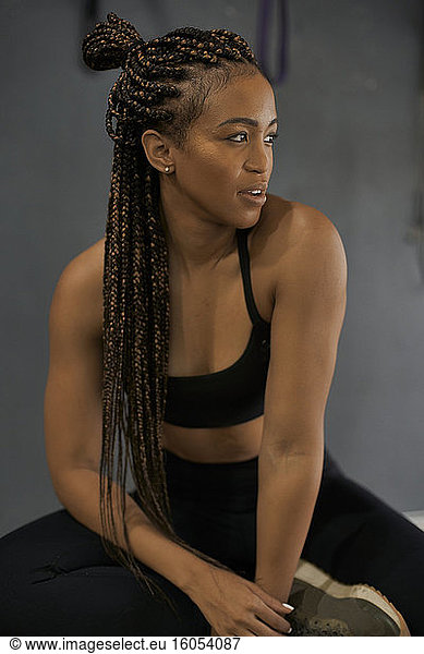 Close-up of thoughtful female athlete with braided hair sitting in gym