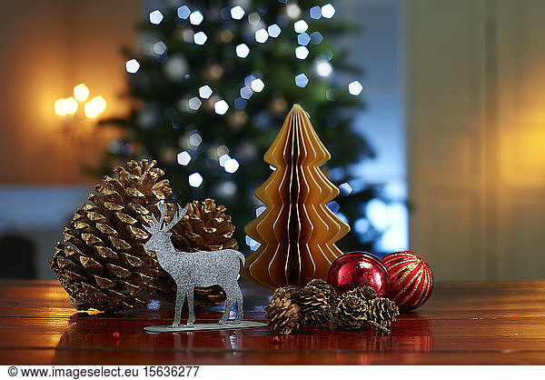 Close-up of various decorations on wooden table with illuminated Christmas tree in background at home