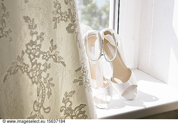 Close-up of wedding sandals by dress on window sill at home