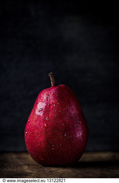 Close-up of wet pear on wooden table against black background