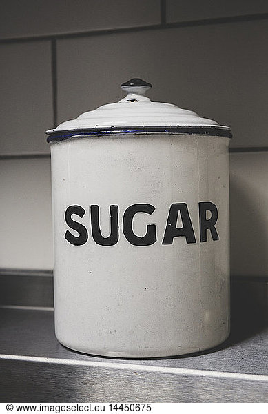Close up of white vintage enamel sugar tin with black lettering.
