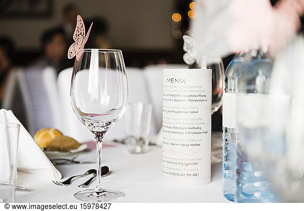 Close-up of wineglass with butterfly decoration and menu on table at wedding reception
