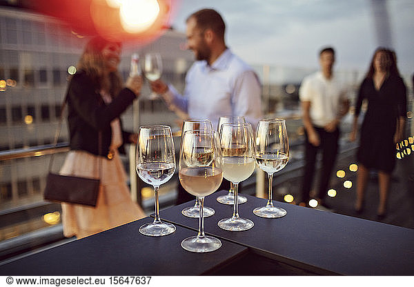 Close-up of wineglasses arranged on table with business professionals in background at terrace during party