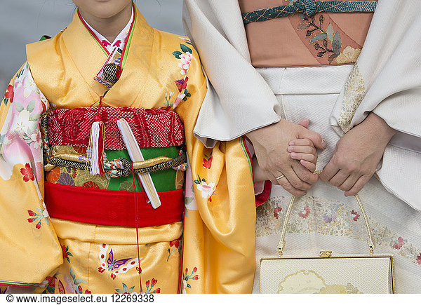 Close up of woman and child holding hands  wearing traditional Japanese kimonos standing side by side  holding smartphones.