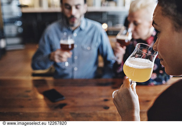 Close-up of woman examining craft beer while sitting with friends at bar