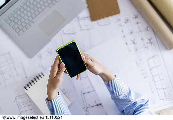 Close-up of woman in office using cell phone with blueprint on table