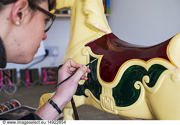 Close up of woman in workshop  painting traditional wooden carousel horse from merry-go-round.