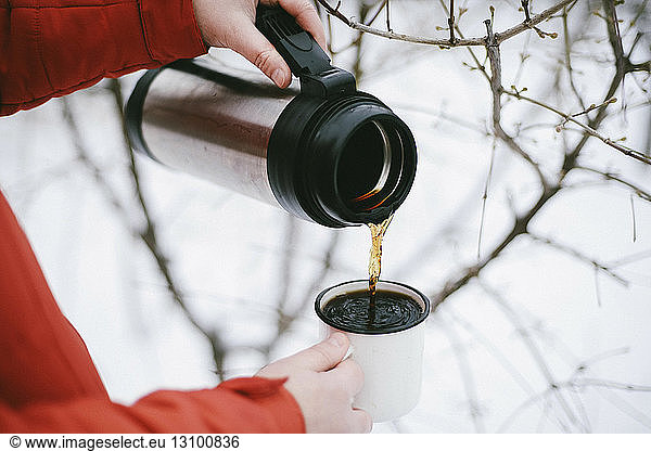 Close-up of woman pouring black coffee from insulated drink container into mug during winter