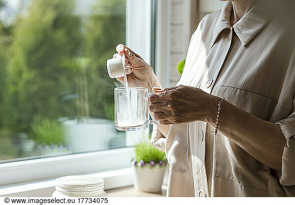 Close-up of woman pouring powder into glass at the window