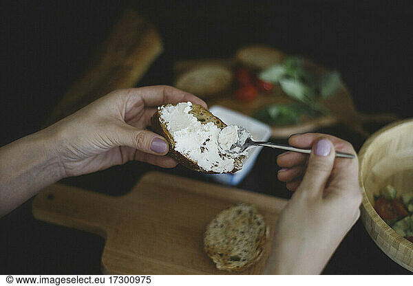 Close up of woman spreads curd cheese on a slice of bread