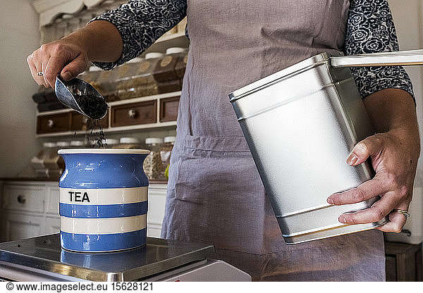 Close up of woman standing in a kitchen  placing loose tea into striped blue ceramic jar.