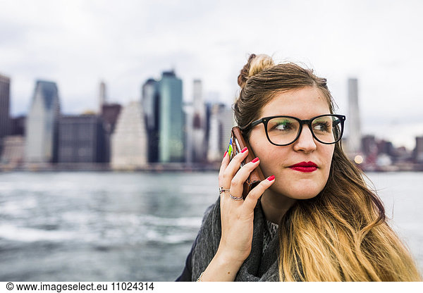Close-up of woman using phone while standing against East River in city