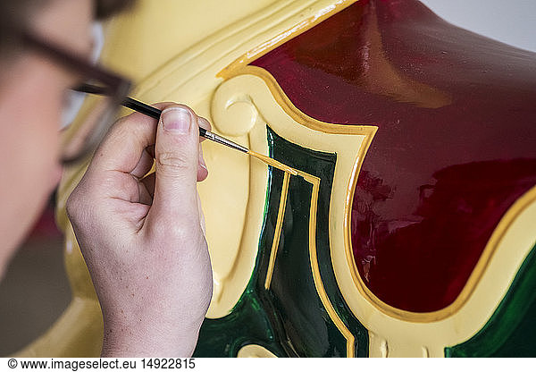 Close up of woman wearing glasses in a workshop  painting traditional wooden horse from merry-go-round.