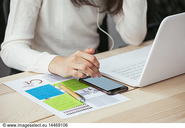 Close-up of woman with document  cell phone and laptop at desk in office