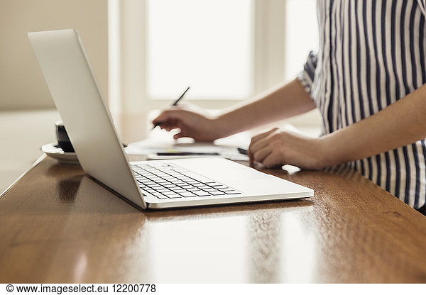 Close-up of woman with laptop and documents on table at home