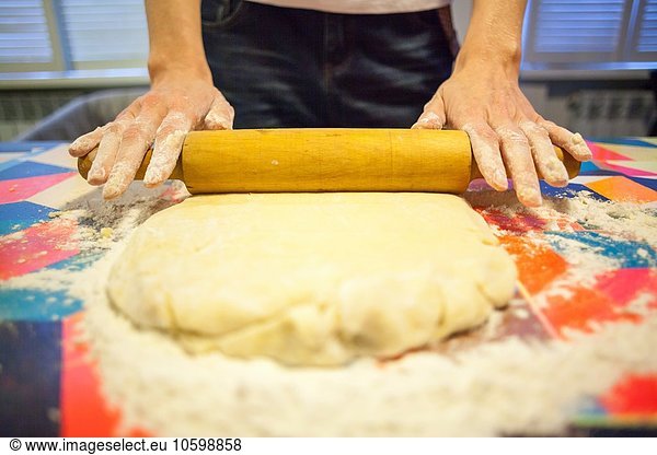 Close up of womans hands rolling dough on kitchen table
