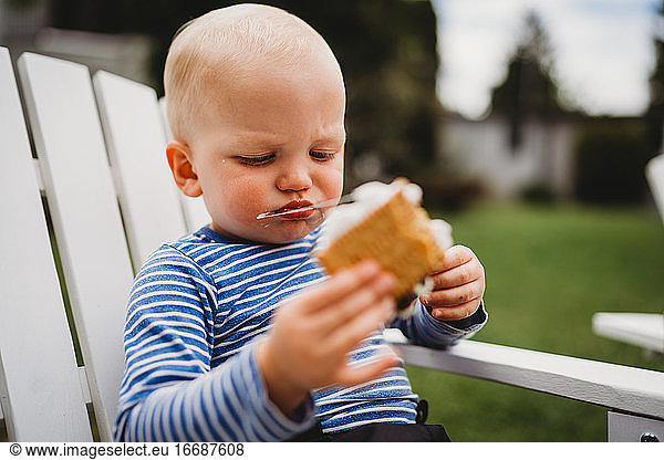 Close up of young boy eating smores with string of melted marshmallows