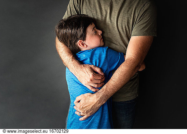 Close up of young boy hugging his father against a black backdrop.