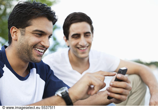 Close-up of young man using mobile phone while friend looking