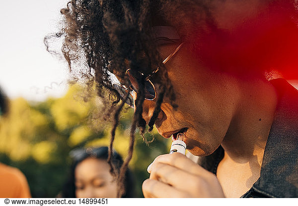 Close-up of young man with curly hair smoking through electronic cigarette
