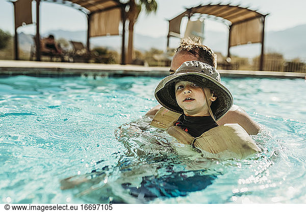 Close up of young toddler boy and father swimming in pool on vacation