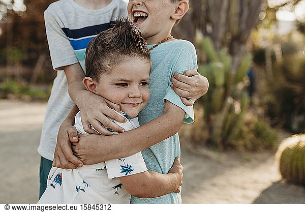 Close up of young toddler boy being hugged by older brothers