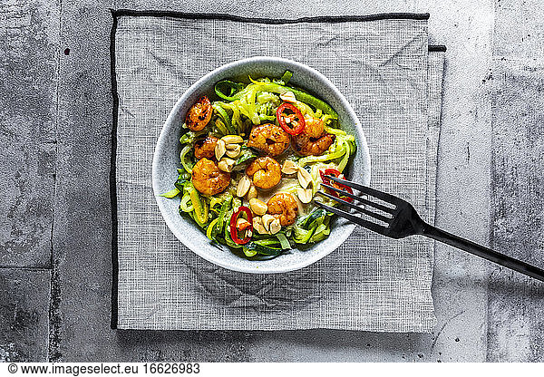 Close-up of zoodles with shrimps and chili served within bowl with fork on table