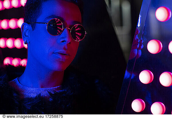 Close up portrait cool young man in sunglasses in neon lighting