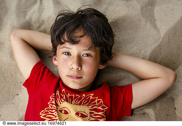 close-up portrait of beautiful boy with bright eyes laying on beach