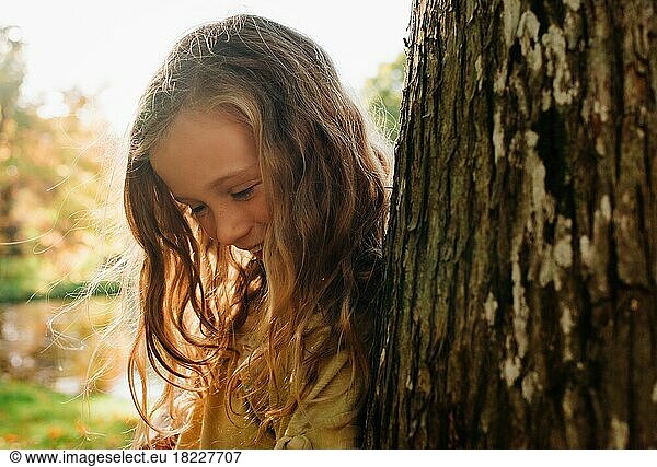 close up portrait of beautiful girl hiding by a tree in golden light
