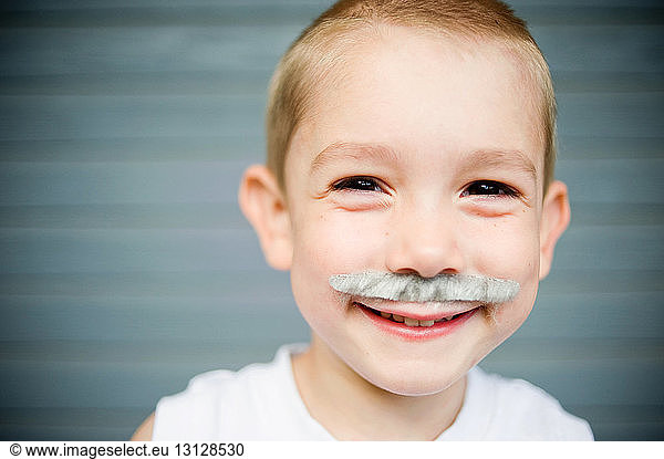 Close-up portrait of happy boy with artificial mustache against wall