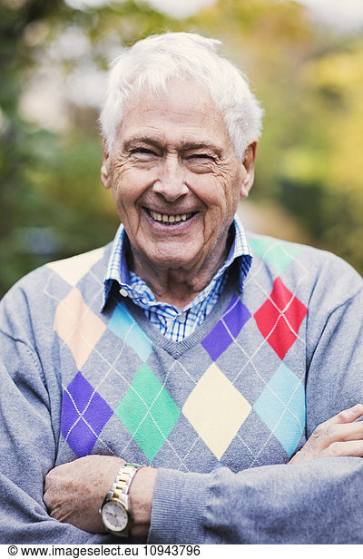 Close-up portrait of happy senior man with arms crossed standing outdoors