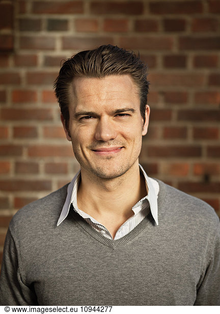Close up portrait of smiling mid adult man in front of brick wall