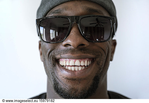 Close-up portrait of smiling young man wearing sunglasses against white background